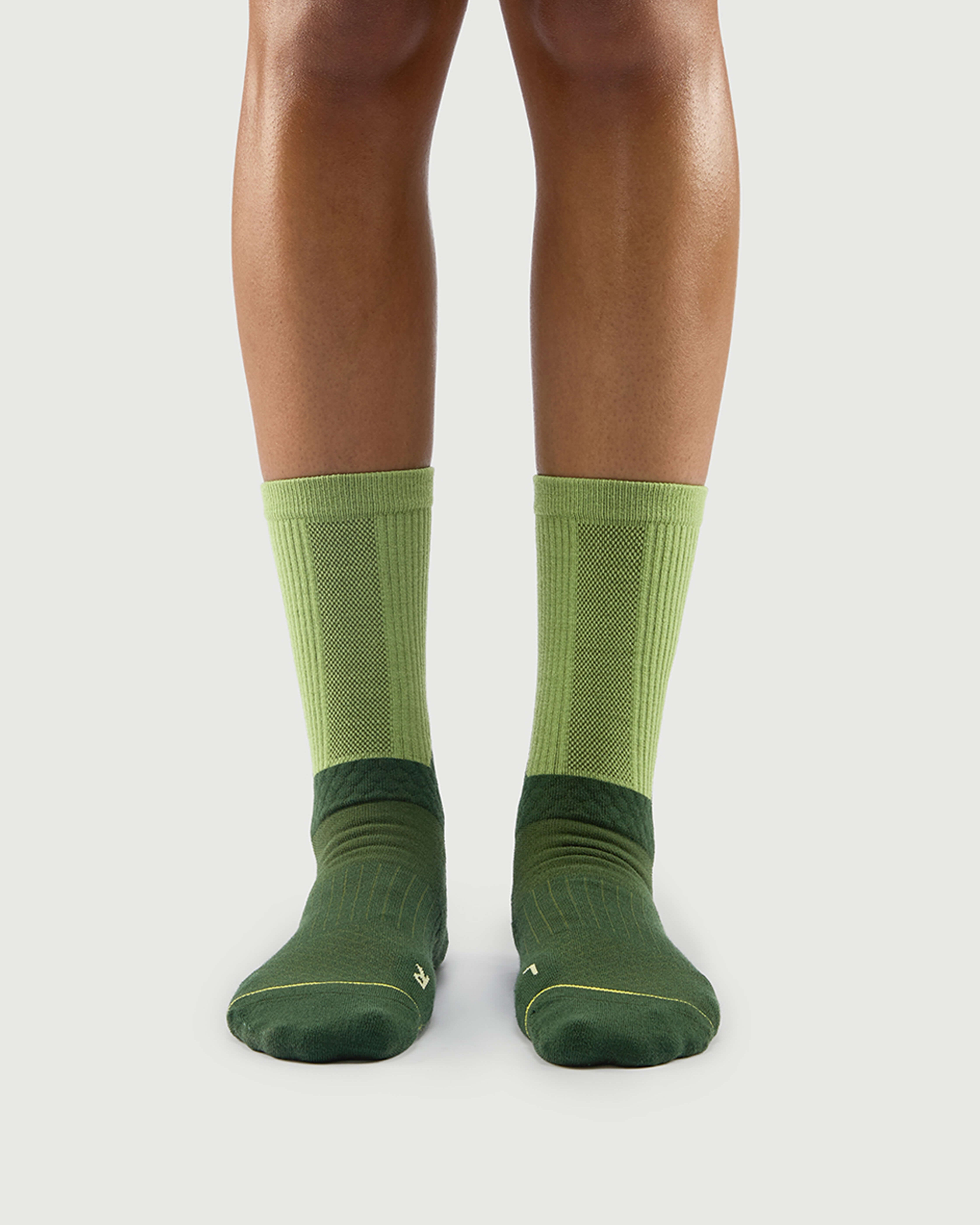 Front view of Crafty Otter socks on a model, featuring dark green and light green two-tone panels.