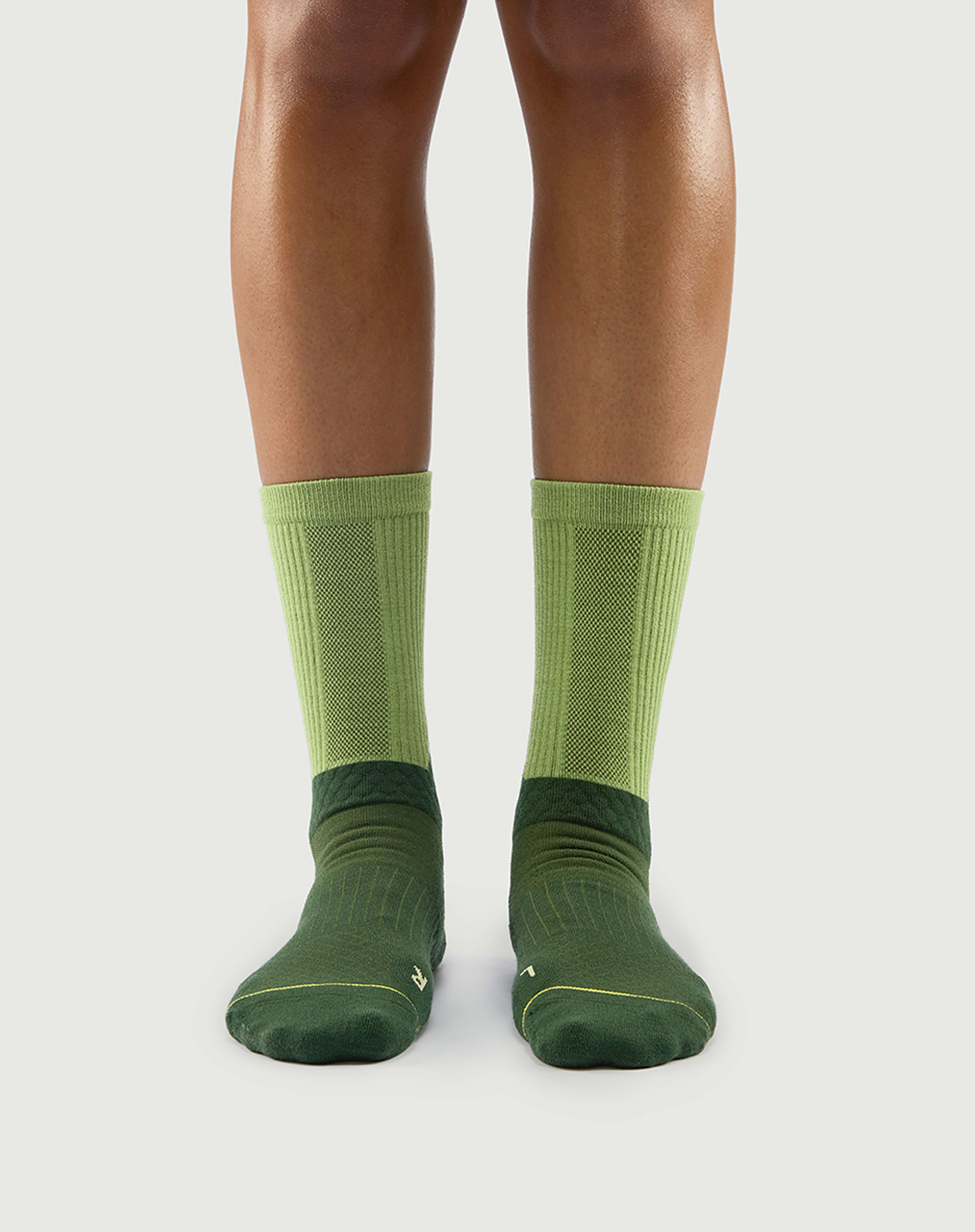 Front view of Crafty Otter socks on a model, featuring dark green and light green two-tone panels.