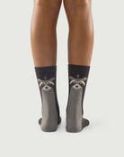 Model wearing grey and black Scrubby Raccoon socks, highlighting the raccoon character on the back.